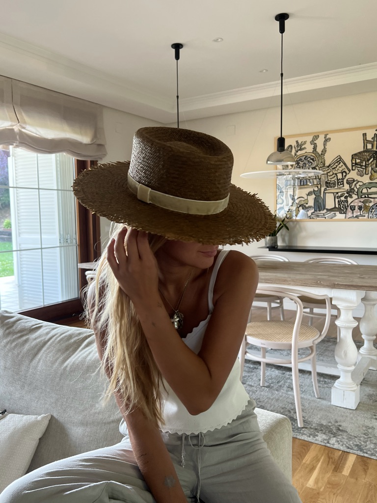 Brown straw hat with a pale ribbon, hand on the brim